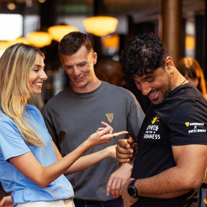 A group of people enjoying a FATTI BURKE "LOVELY DAY FOR A GUINNESS" BLACK T-SHIRT from Guinness Webstore UK at a bar.