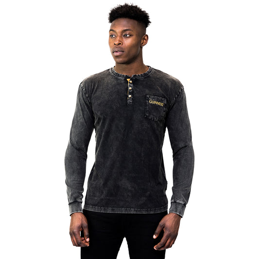 A man faces forward wearing a faded black Guinness Classic Henley long sleeve shirt with collar buttons and a logo on the chest pocket, set against a white background.