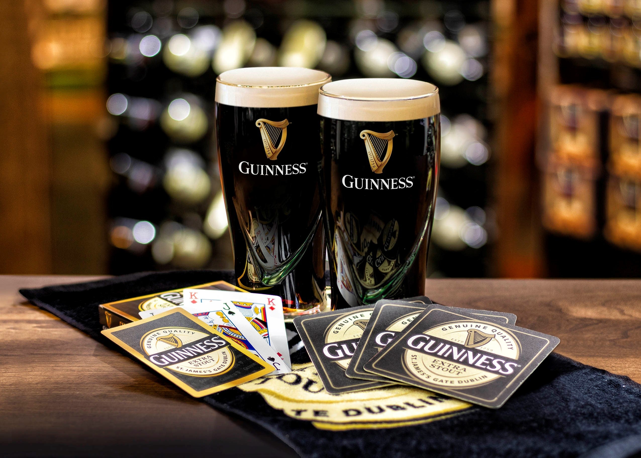 Two Guinness UK pints and playing cards on a table.