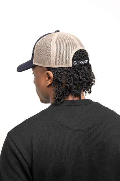 A person in a black shirt and a Guinness Checked Trucker Cap with an adjustable strap, featuring "Guinness" on the back, stands facing away—a subtle nod to Irish heritage. Available at Guinness Webstore UK.