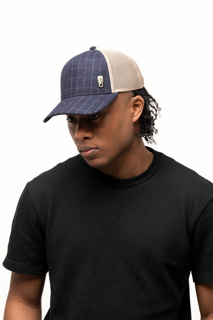 A person wearing a black t-shirt and the Guinness Checked Trucker Cap by Guinness Webstore UK, featuring a denim-textured navy design with a small pin, stands against a plain white background.