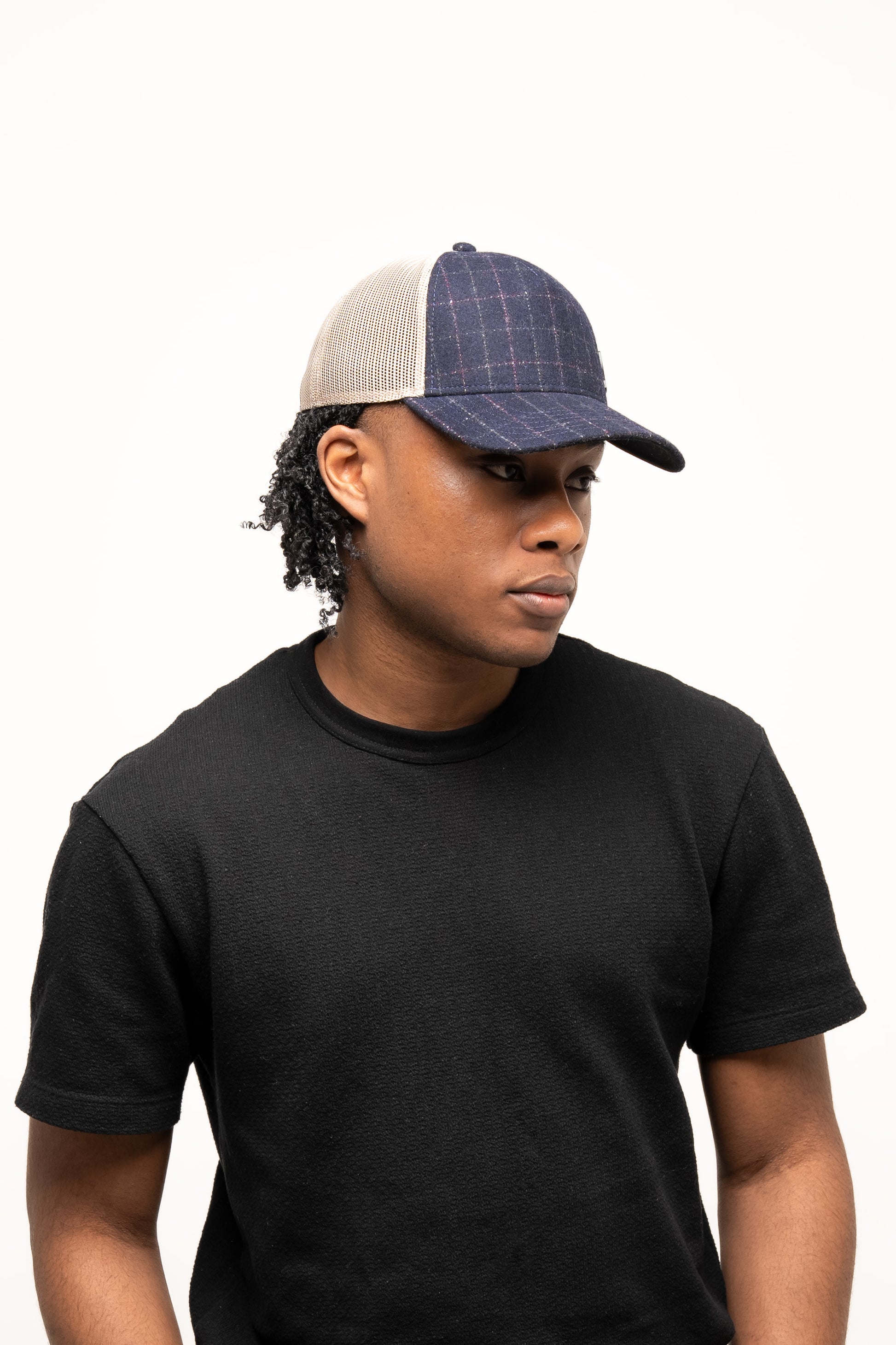 Person wearing a black t-shirt and the Guinness Checked Trucker Cap from Guinness Webstore UK, featuring blue plaid, a beige mesh back, and an adjustable strap, standing against a plain white background.