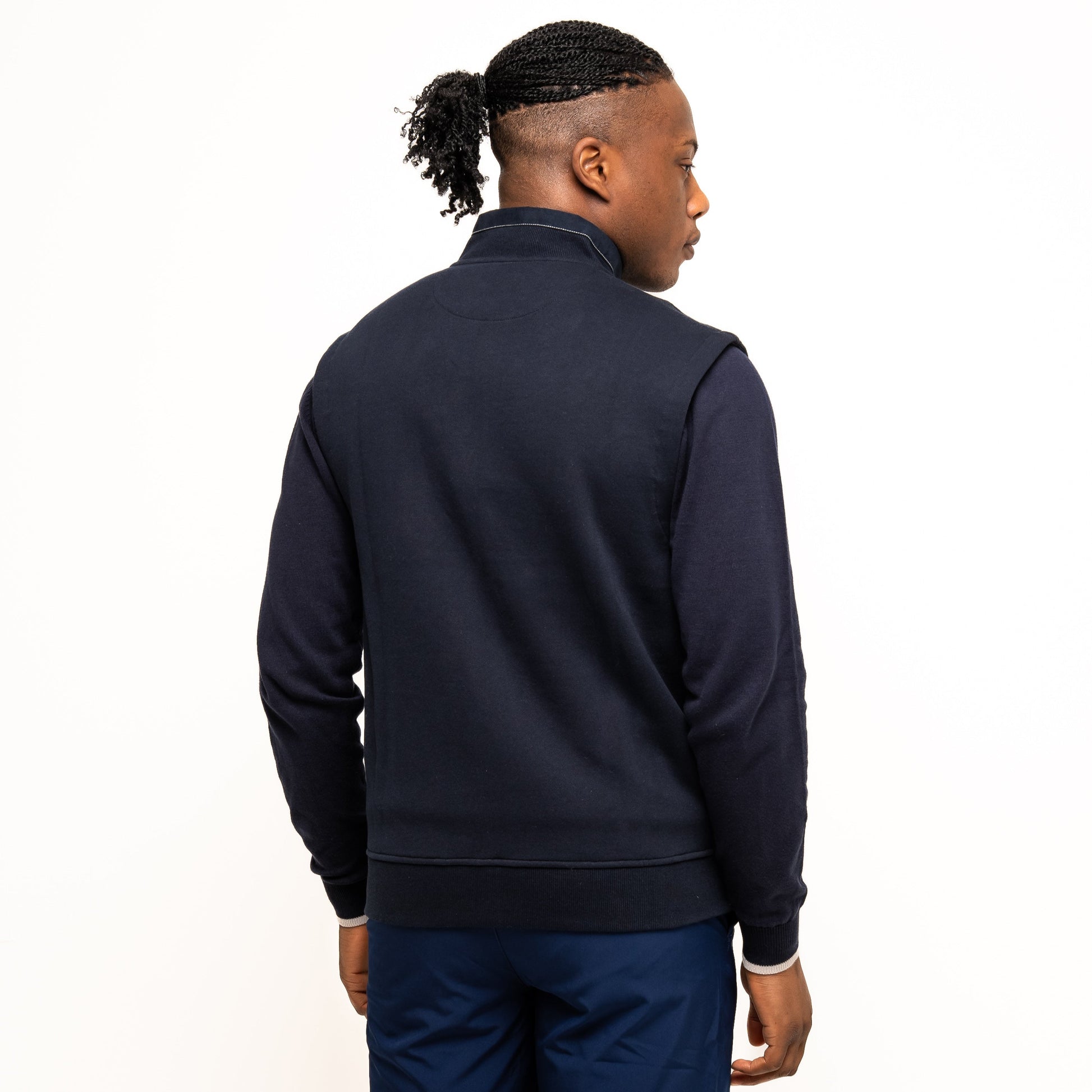 A person stands facing away, wearing the Guinness Performance Gilet from Guinness Webstore UK and navy shorts against a plain white background.