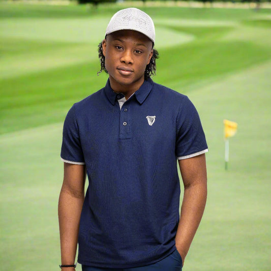 Wearing the Guinness Performance Polo - Navy by Guinness Webstore UK, along with navy shorts and a light gray cap, a person stands against a plain white background, one hand in their pocket.
