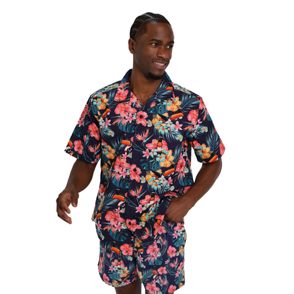 A man wearing eco-friendly fabric, navy blue Hawaiian shirt, and matching Guinness Toucan Hawaiian Beach Shorts from Guinness Webstore UK adorned with vibrant floral patterns. He has one hand in his pocket and is looking to the side while smiling.