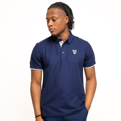 A man in the Guinness Performance Polo - Navy from Guinness Webstore UK and matching shorts stands with one hand in his pocket, looking to the side. The polo’s premium double pique fabric provides all-day comfort against a white background.