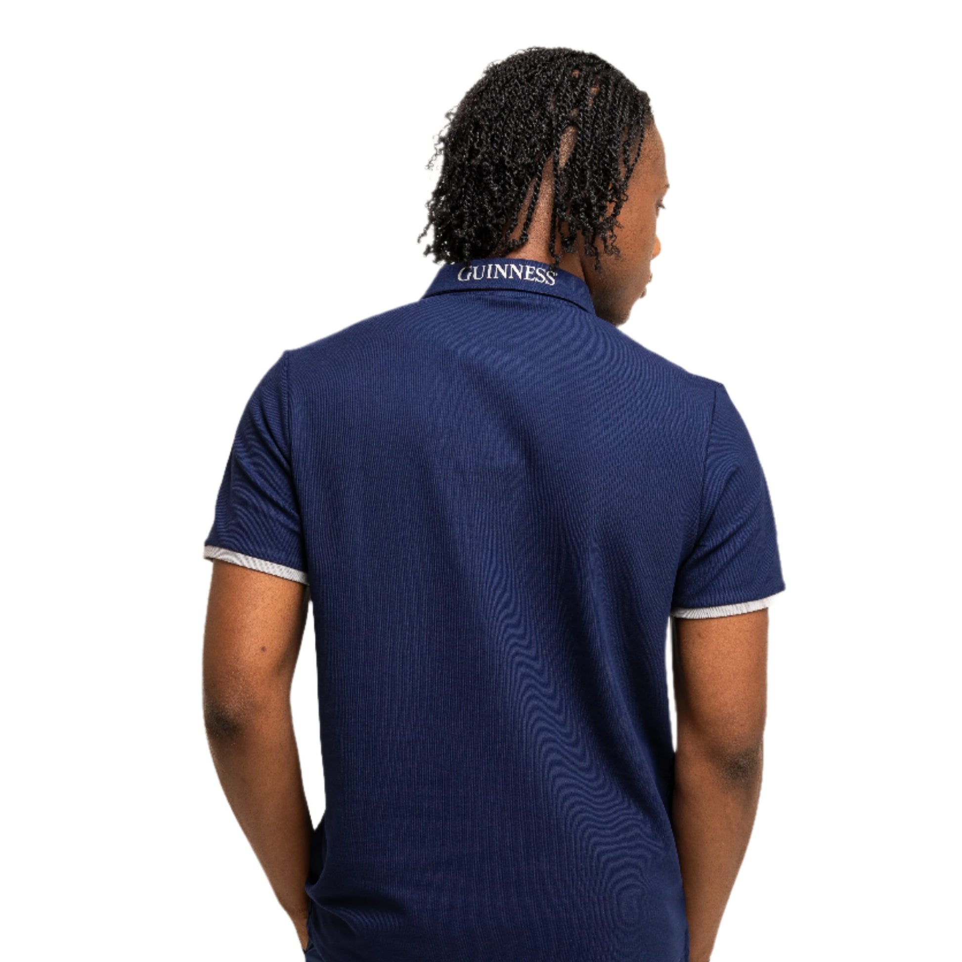 A person faces away in the Guinness Performance Polo - Navy from Guinness Webstore UK, featuring "GUINNESS" on the collar and matching navy shorts, showcasing classic style against a plain white background.