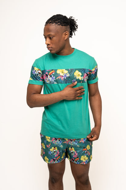 A man in eco-friendly Guinness Toucan Hawaiian Green Beach Shorts by Guinness UK stands against a plain white background, looking to his left with one hand on his chest.