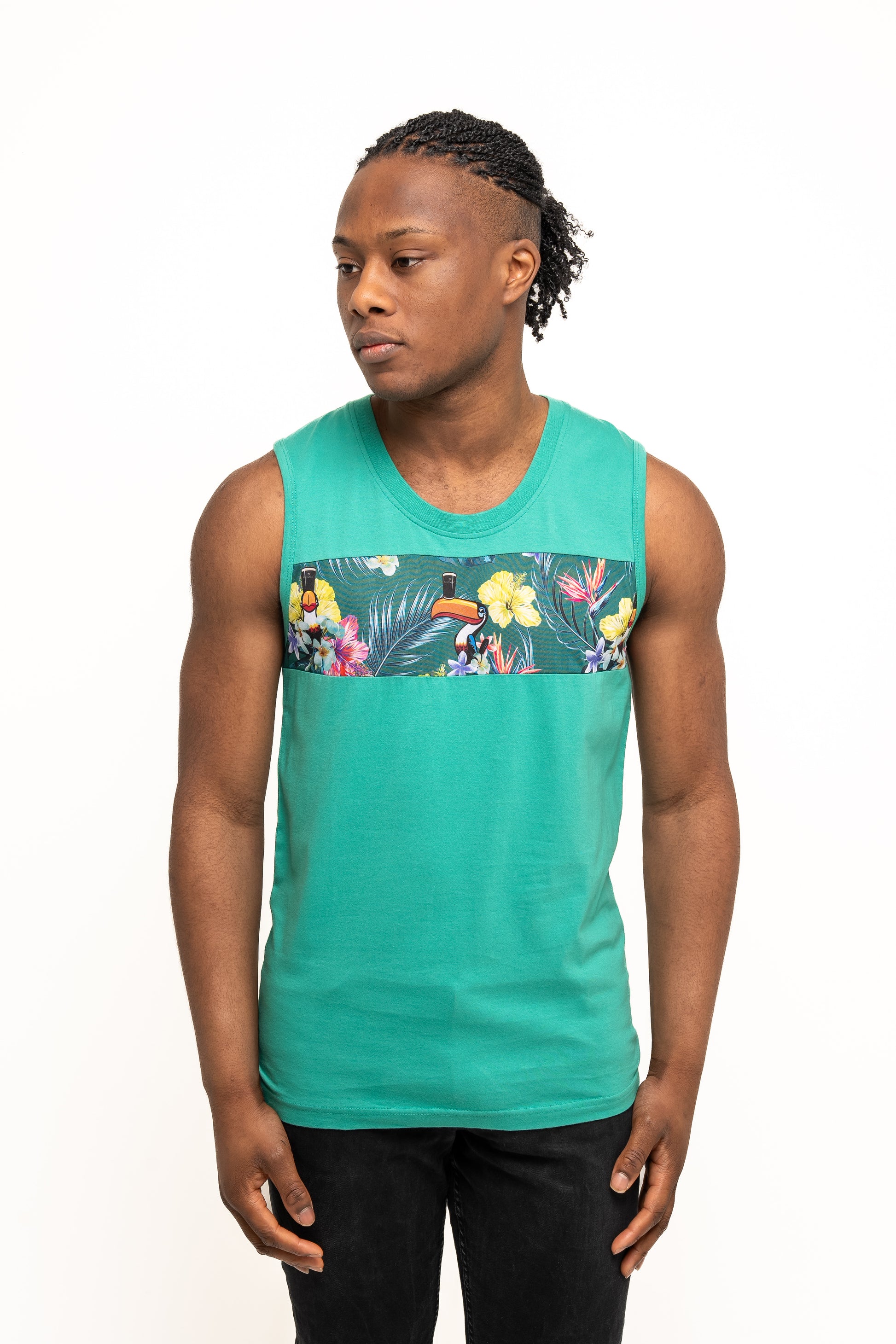 A man in the Guinness Toucan Hawaiian Green Tank from Guinness Webstore UK, featuring a floral and toucan chest design, stands slightly turned against a plain white background, channeling true tropical paradise vibes.