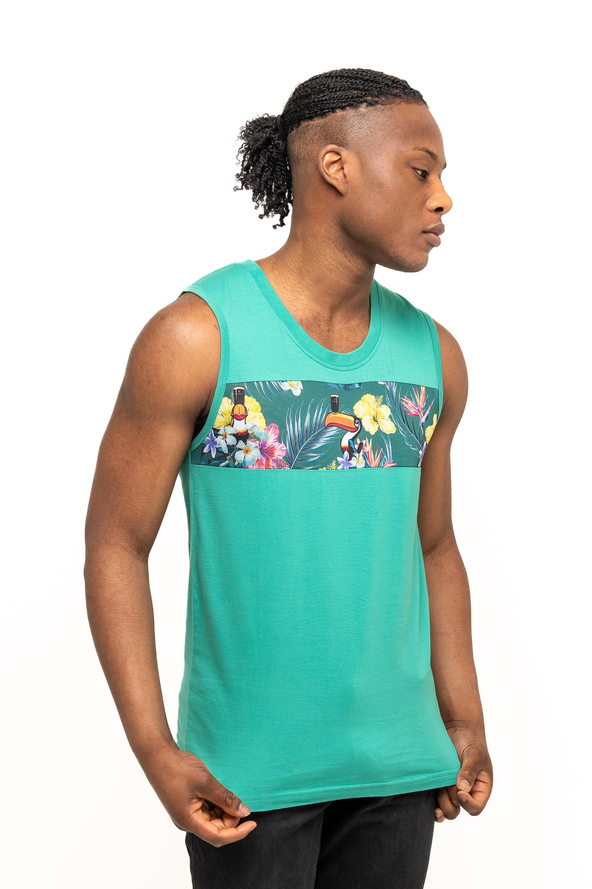 A man wearing the Guinness Toucan Hawaiian Green Tank from Guinness Webstore UK, featuring a tropical floral print across the chest, stands against a white background, embodying vibrant paradise vibes.