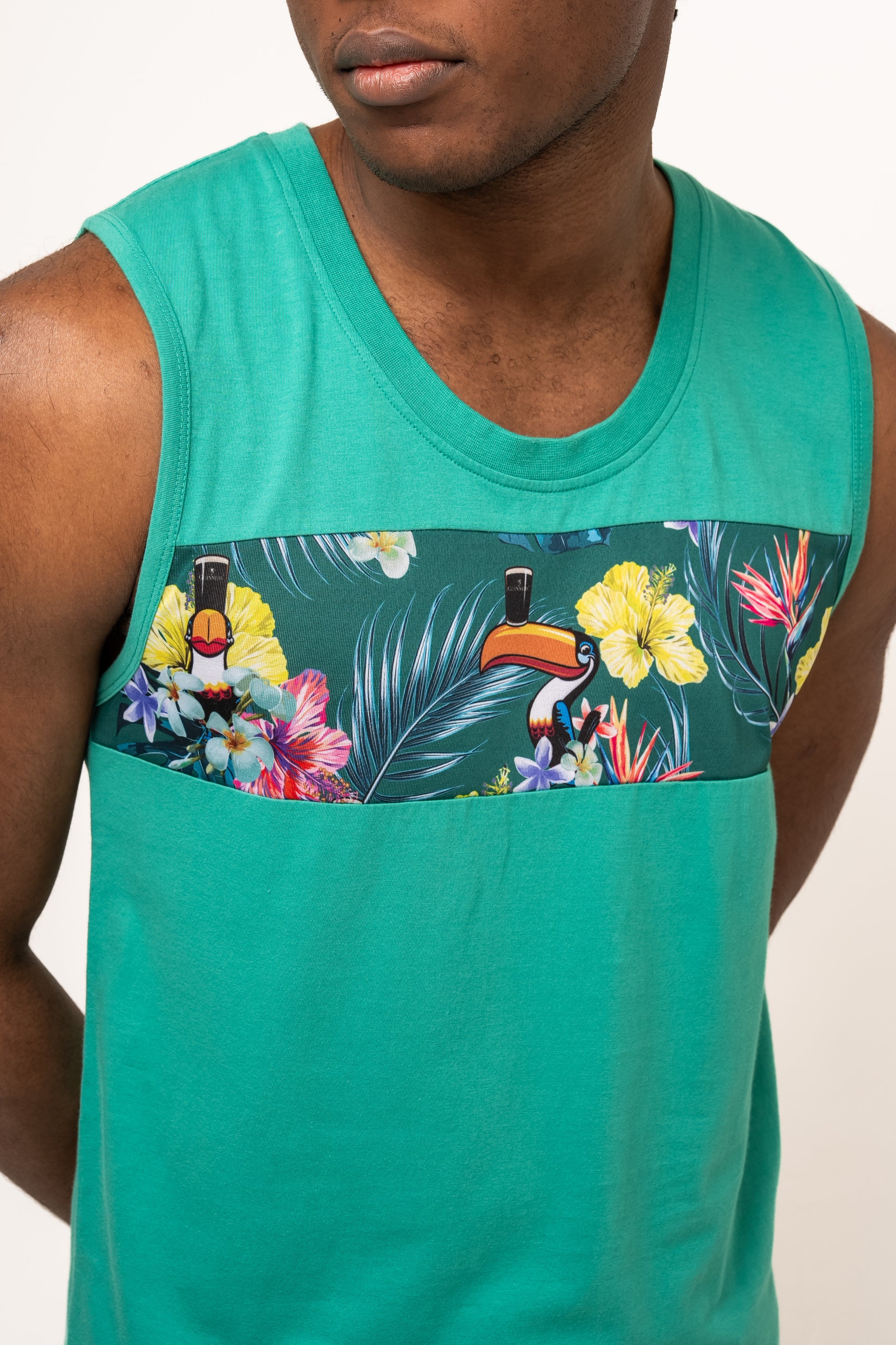 Wearing the Guinness Toucan Hawaiian Green Tank from Guinness Webstore UK, with its sleeveless teal style and vibrant chest panel of flowers and toucans, brings tropical paradise vibes.