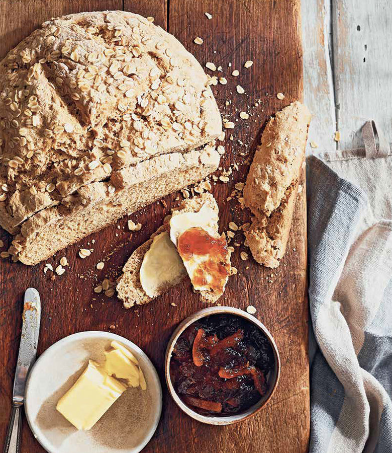 An Official Guinness UK Hardcover Cookbook filled with delicious recipes displayed alongside a wooden cutting board adorned with bread and butter.