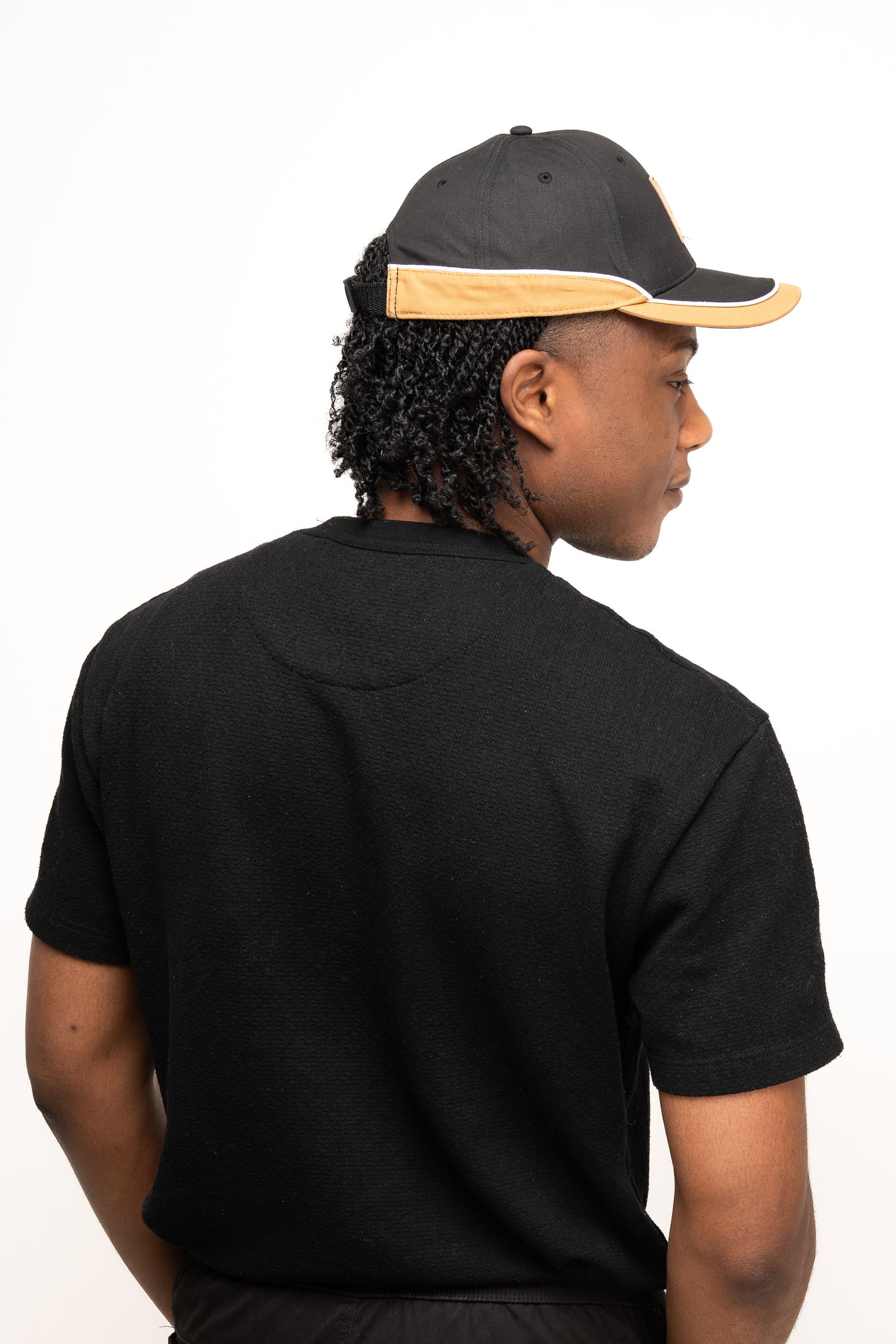 Someone wearing a black t-shirt and the Guinness Black Cap with Caramel Edge from Guinness Webstore UK is facing away from the camera, displaying the cap's distinctive look along with part of their right profile.