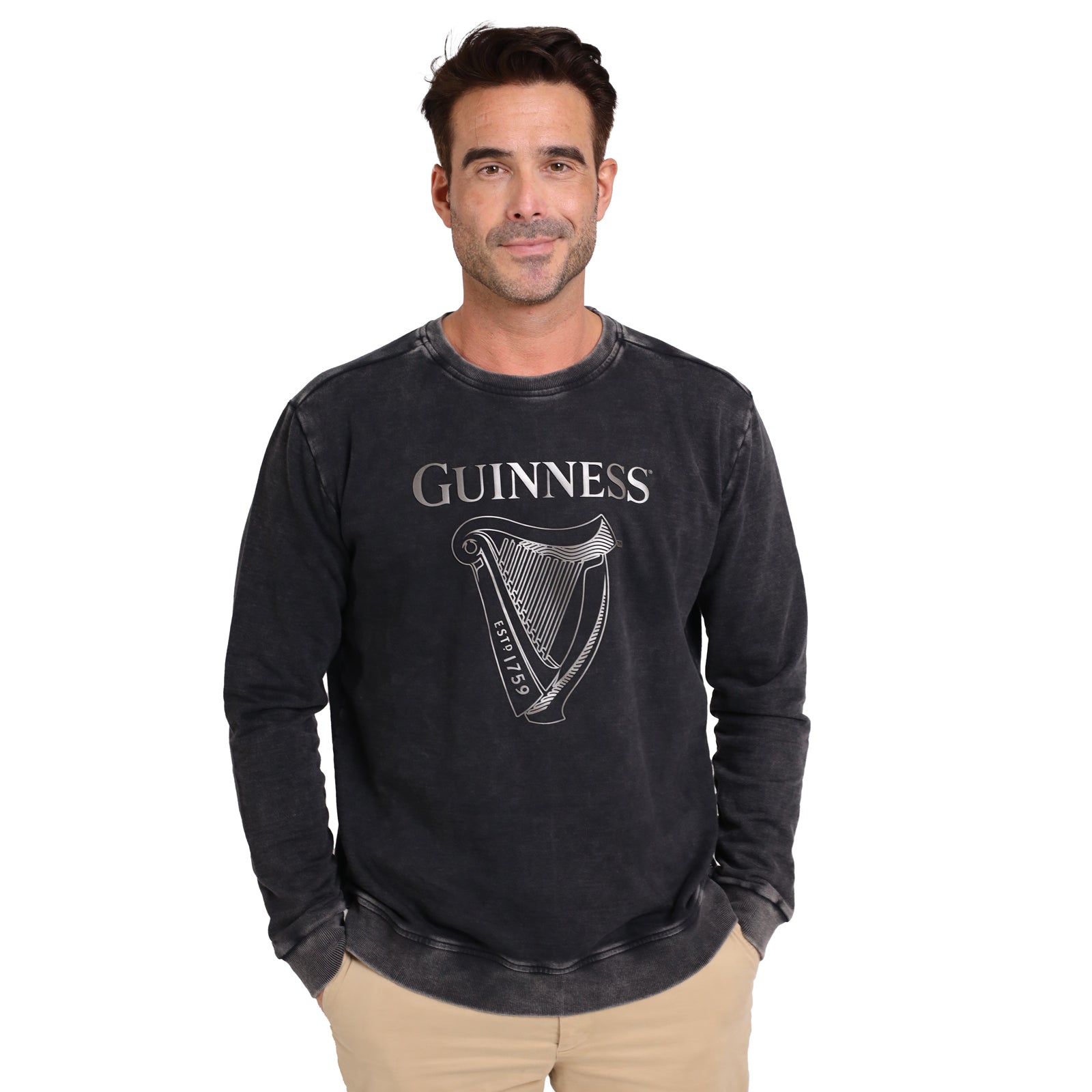 A man faces forward wearing the Guinness Metallic Print Trademark Sweatshirt by Guinness Webstore UK, featuring a metallic harp graphic and sustainable cotton, paired with beige pants against a plain white background.