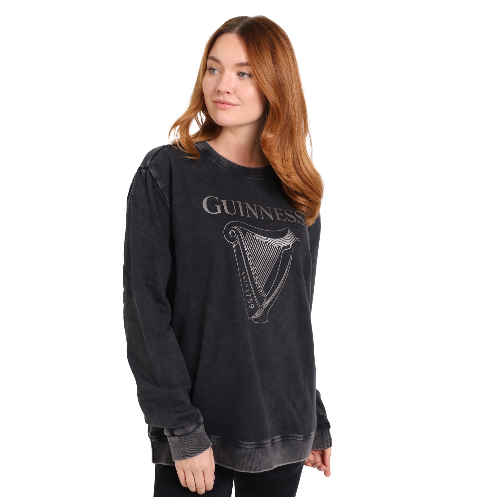 A woman with long red hair wears the Guinness Metallic Print Trademark Sweatshirt from Guinness Webstore UK, featuring a metallic harp logo, standing against a plain white background.