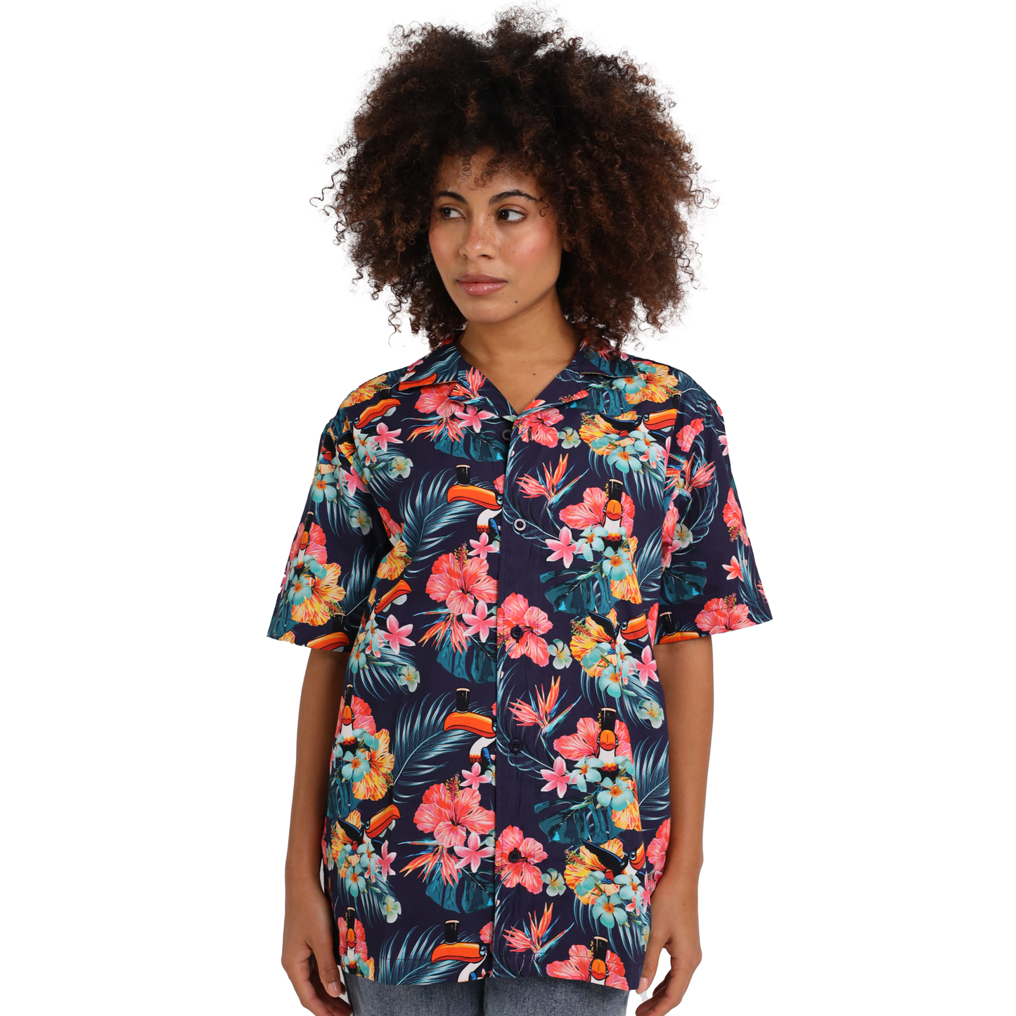 A person with curly hair is wearing a navy blue short-sleeved, button-up shirt boasting a colorful floral pattern, exuding tropical paradise vibes. They're looking to the side in their Guinness Toucan Hawaiian Shirt by Guinness, made from 100% cotton.