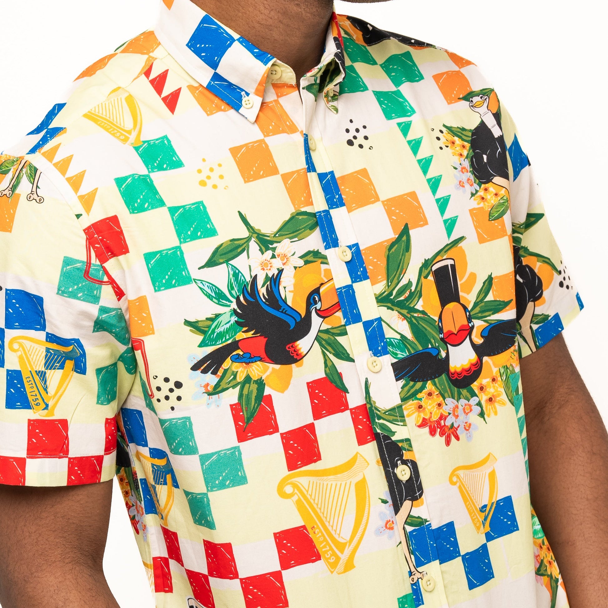A person wearing the Guinness Toucan Beach Shirt by Guinness Webstore UK—a Hawaiian-style, short-sleeved button-up featuring a colorful toucan, harp, and foliage pattern on breathable woven cotton for comfort.