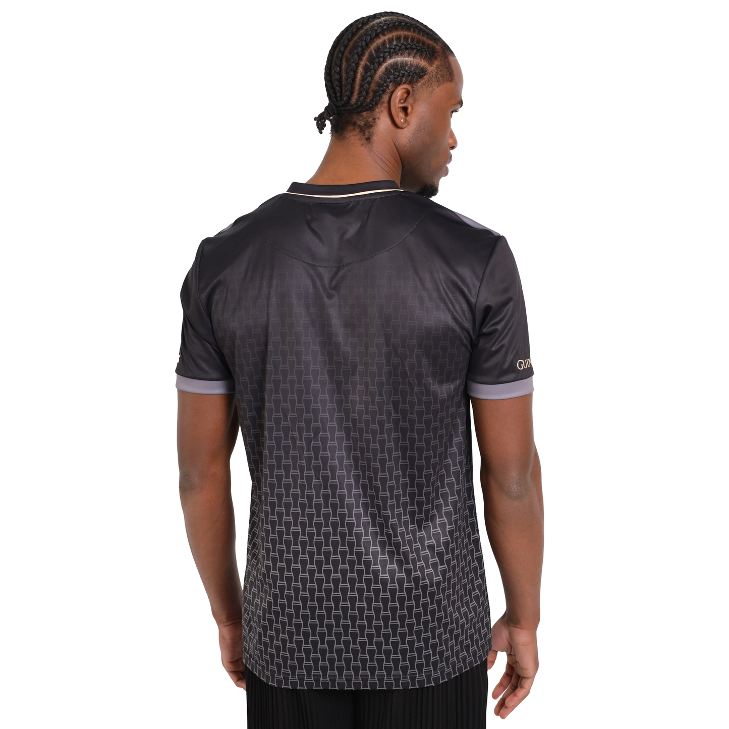 A man faces away in a Guinness Football Jersey, featuring a black base with discreet geometric patterns and contrasting trim.