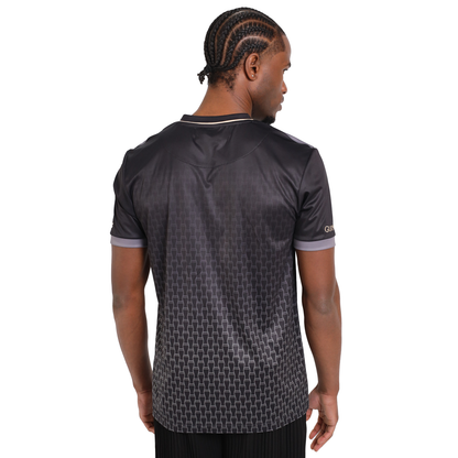 A man faces away in a Guinness Football Jersey, featuring a black base with discreet geometric patterns and contrasting trim.