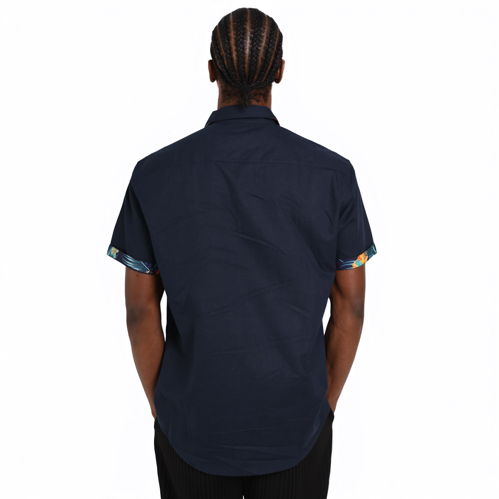 A person with braided hair is shown from the back wearing a short-sleeve Guinness Navy Linen Summer Shirt from Guinness Webstore UK, featuring patterned sleeve cuffs.