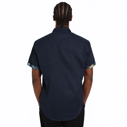 A person with braided hair is shown from the back wearing a short-sleeve Guinness Navy Linen Summer Shirt from Guinness Webstore UK, featuring patterned sleeve cuffs.