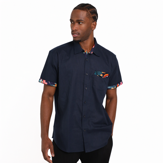 A man stands against a plain white background wearing the Guinness Navy Linen Summer Shirt from Guinness Webstore UK, a short-sleeve button-up featuring colorful patterned accents on the cuffs and pocket.