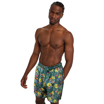 A shirtless man with an athletic build and braided hair stands wearing Guinness Toucan Hawaiian Green Beach Shorts by Guinness UK, featuring a vibrant floral pattern. The background is plain white.