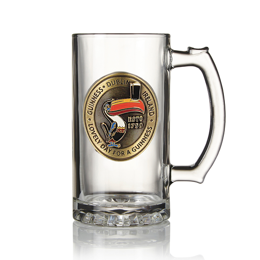 Clear glass collectible drinkware with a large handle and a decorative badge featuring the iconic Guinness Gilroy Toucan Tankard design by John Gilroy, displaying the text "Guinness Dublin Ireland," "Estd 1759," and "Lovely Day For A Guinness" on its front is available on Guinness Webstore UK.