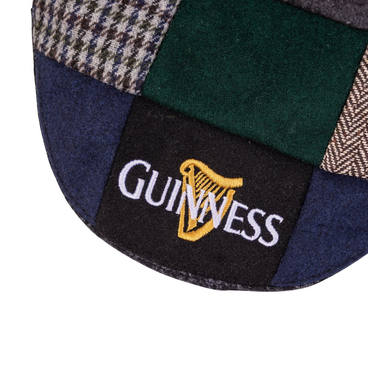 Close-up of a Guinness Tweed Cap with traditional Irish design, featuring a Guinness logo embroidered in gold on a black tag.