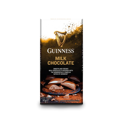 A Guinness Luxury Milk Chocolate Bar with chunks of milk chocolate displayed on a brown backdrop. The packaging, which is part of the official Guinness merchandise, showcases the iconic logo and text that emphasizes the bar's rich flavor notes.