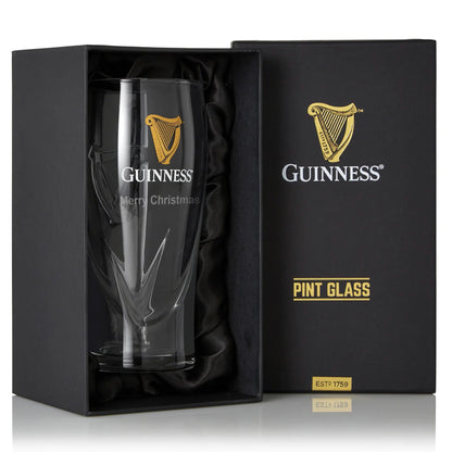 The Guinness UK Pint Glass - 2 Pack comes in a black gift box, featuring the golden harp logo and "Merry Christmas" text, making it an exquisite addition to any beer glass collection—perfect for celebrating the season.