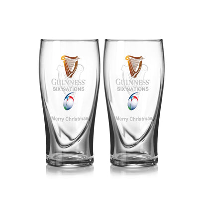 The Guinness Six Nations Pint Glass - 2 Pack features two clear glasses adorned with the official Six Nations logo and "Merry Christmas" text, along with a harp and rugby ball design, perfect for enhancing your rugby viewing experience.