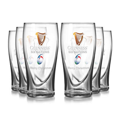 The Guinness Six Nations Pint Glass 6 Pack features six clear glasses with "Merry Christmas" text and a rugby ball logo, arranged in two rows. Perfect for any rugby enthusiast's festive celebrations.