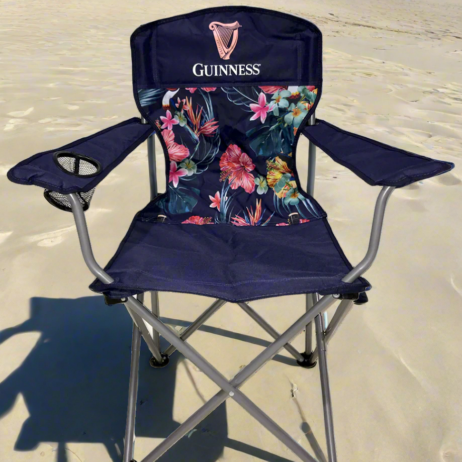 The Guinness Toucan Hawaiian Beach Chair from Guinness Webstore UK rests on sandy ground with its tropical floral pattern and can pair perfectly with a cooler backpack from the new Guinness Hawaiian collection.