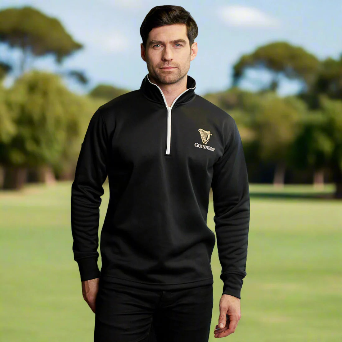 A man in a Guinness UK Harp Half Zip Top stands outdoors in a grassy area with trees in the background, enjoying the benefits of its moisture-wicking properties.