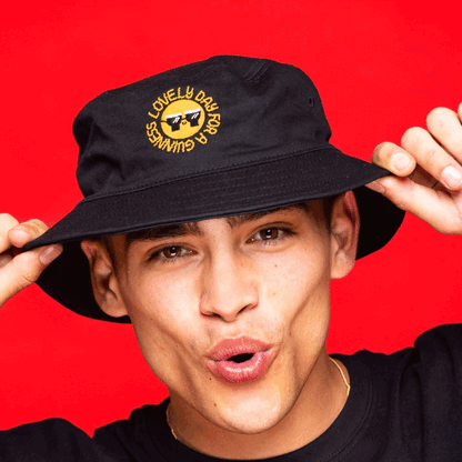 A man wearing a FATTI BURKE "LOVELY DAY FOR A GUINNESS" bucket hat from Guinness Webstore UK, perfect for the festival season with a smile on it.