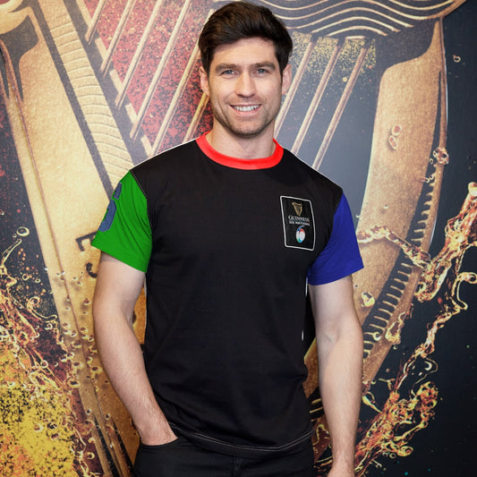 A man in a black t-shirt, wearing the Guinness UK Six Nations Premium Colour Block T-Shirt, is posing in front of a harp.