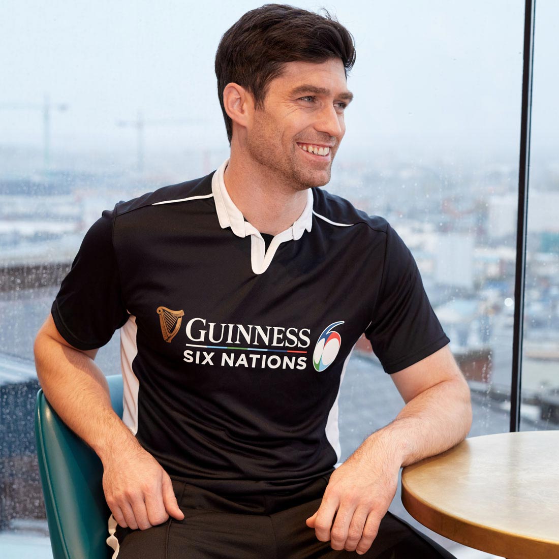 A Guinness UK Six Nations fan sitting at a table wearing a Guinness 6 Nations Performance Rugby Jersey.