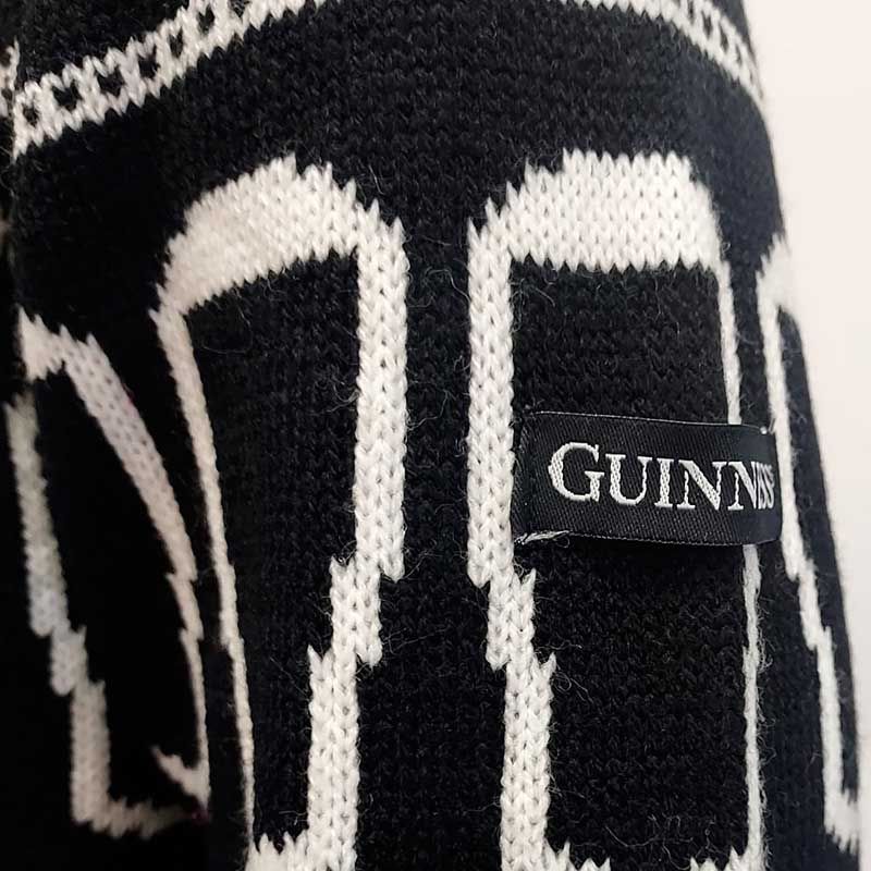 Close-up of a black and white patterned knit fabric featuring a label that reads "Guinness UK," evoking the festive charm of the Guinness Festive Pints Christmas Jumper.