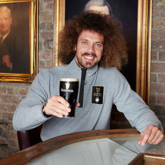 A man with curly hair enjoying a pint of Guinness® during the Six Nations Grey Half Zip Fleece.