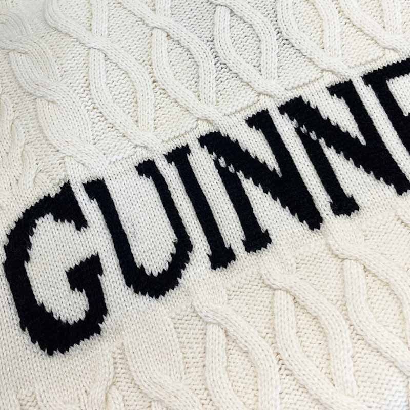 Close-up of a white knit fabric featuring the bold black letters "GUINNESS" across the center, embodying the classic Aran style. This piece, reminiscent of the Guinness Cream Cable Knit Jumper by Guinness, is a true winter essential with cozy charm.