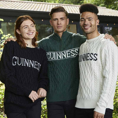 Three individuals smiling and standing outside, all wearing the Guinness Cable Knit Jumper—a cream-colored Aran-style essential from Guinness, ideal for any cold-weather adventure.