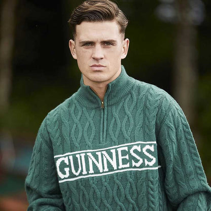 Person wearing a Guinness Green Cable Knit Quarter Zip Jumper with "GUINNESS" written on the front.