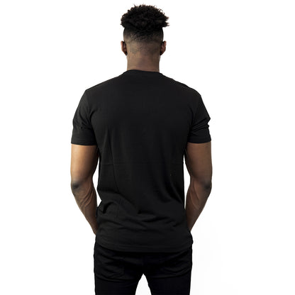 A man faces away from the camera, wearing a Guinness® Distressed Gaelic Label T-Shirt by Guinness UK and black pants, set against a white background.