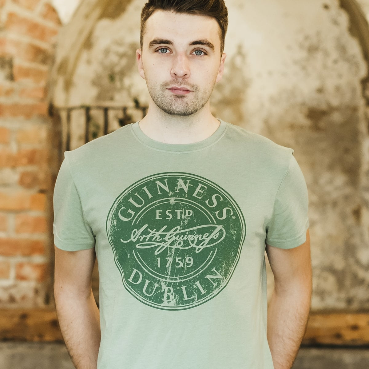 A man wearing a Guinness Green Bottle Cap T-shirt, holding a bottle cap.