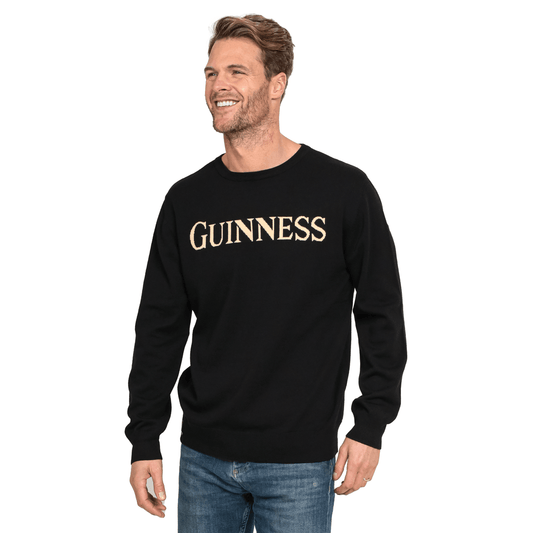 A man wearing a black sweater with the word "Guinness" on it, made of Guinness UK's 100% Organic Cotton Jumper.