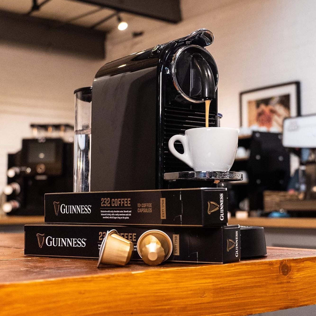 A Guinness UK-branded Guinness 232 Coffee Capsules machine sits on a table in a coffee shop.