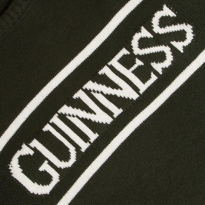 Close-up of the word "Guinness" embroidered in white on a Guinness UK Bottle Green Crew Neck Jumper background.