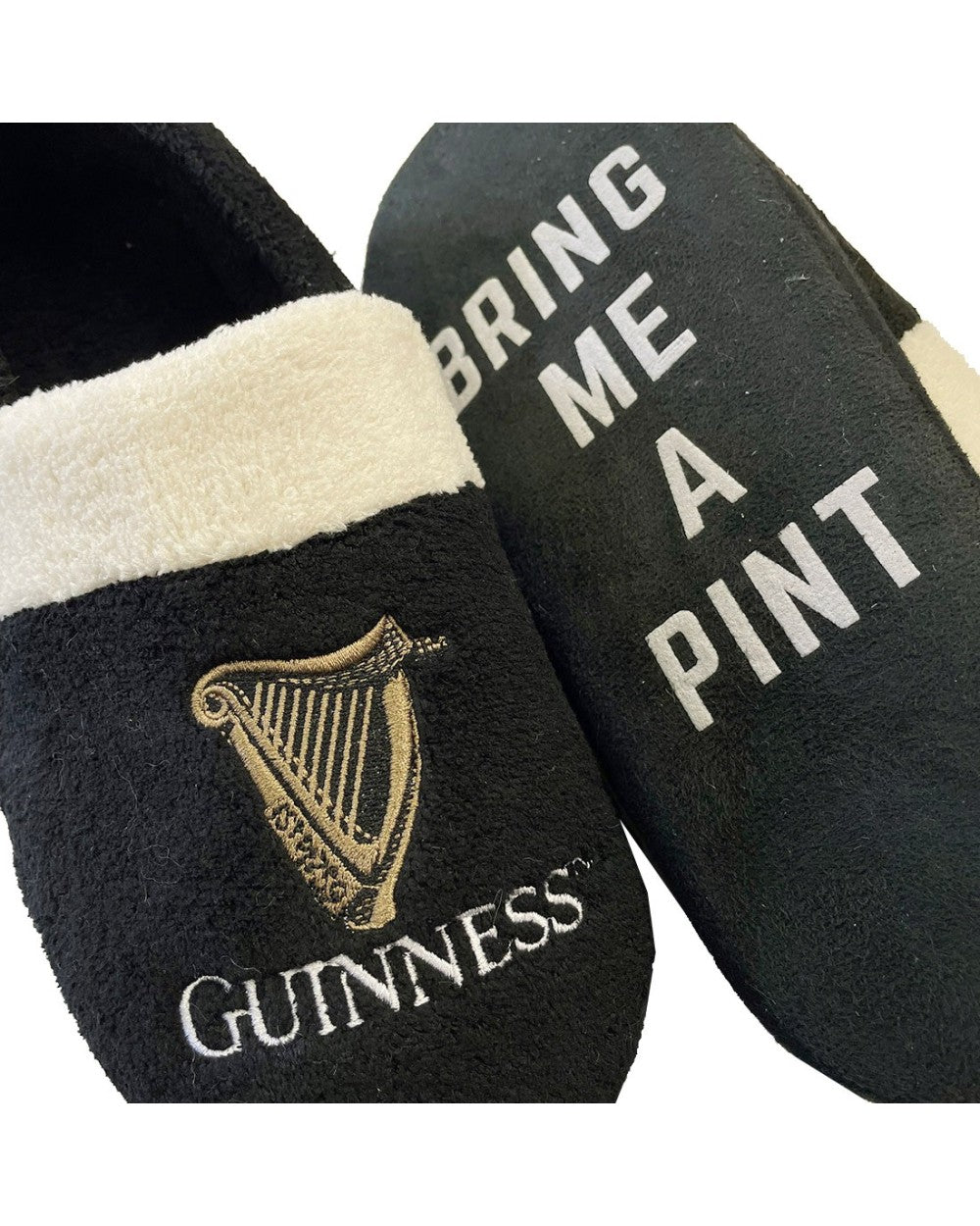 These Guinness Harp Slippers - Bring A Pint are perfect for beer enthusiasts. Featuring a sleek black design with a white lining, one slipper displays the iconic Guinness logo while the other boldly proclaims, "BRING ME A PINT." They're ideal for lounging in style and showcasing your love for a good brew.