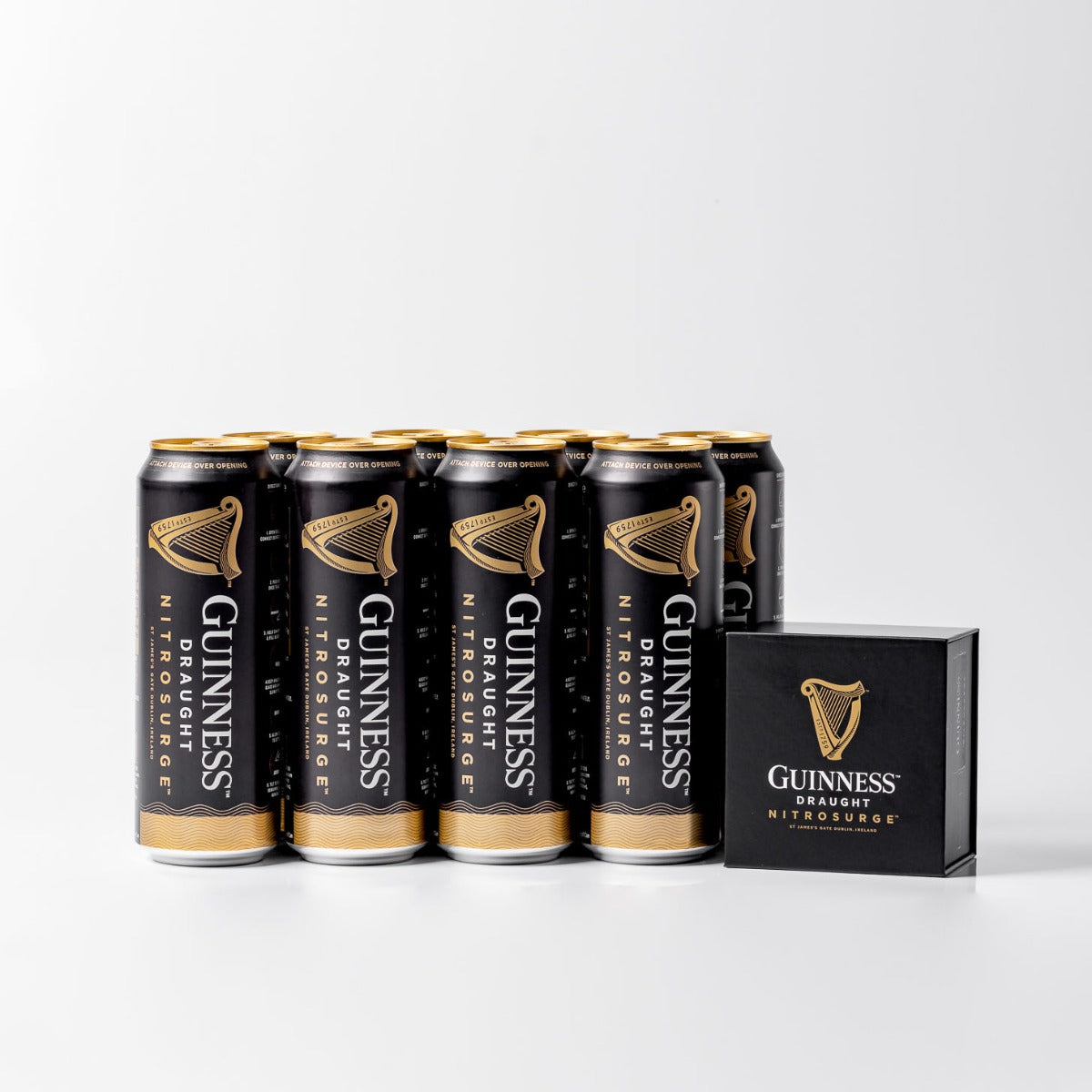 A stack of Guinness Nitrosurge Gift Bundle cans, crafted by Guinness UK with cutting-edge NITROSURGE technology, is elegantly displayed next to a Guinness box on a light background, offering the promise of a perfect pour with smooth nitrogen bubbles.